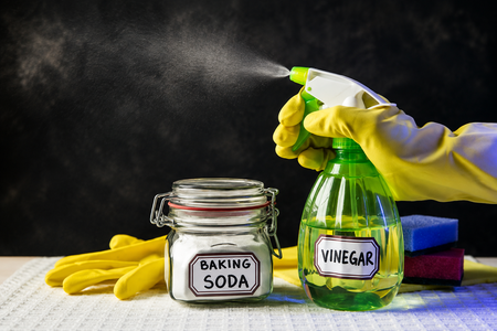 Baking soda, vinegar spray bottle, cleaning sponges and yellow rubber gloves