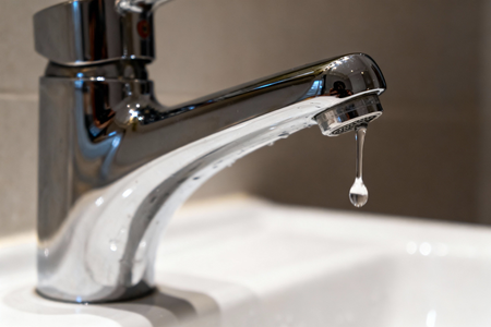 Close-up of a bathroom faucet with a single drop of water dripping from the spout