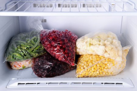 Bags of frozen green beans, berries, cauliflower and corn stored in a home freezer