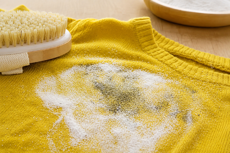 Baking soda sprinkled on a yellow sweater with a cleaning brush nearby